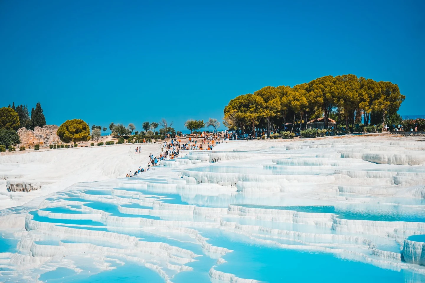 White travertine terraces and turquoise pools at Pamukkale, Türkiye. Photo: Ne Hayaldesin / Pexels; a real photograph, not a promise that every basin will be full during a visit.