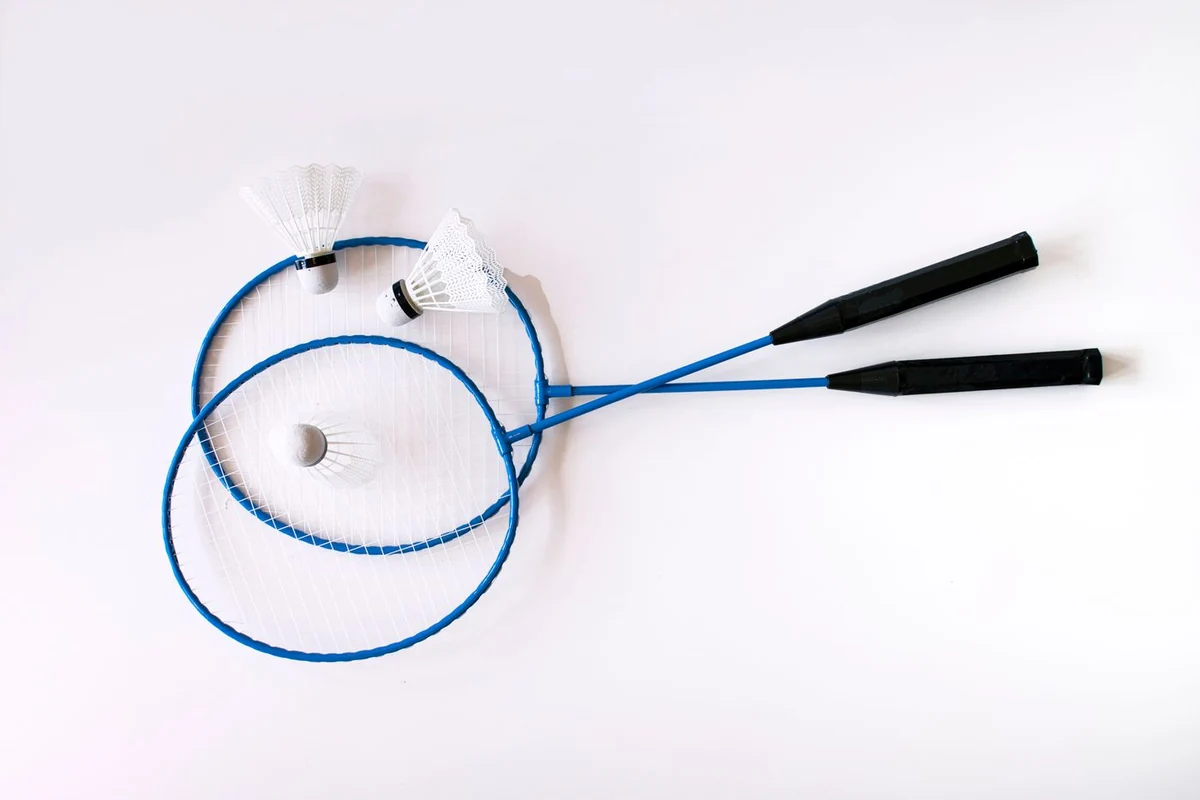 Two blue badminton rackets and three synthetic shuttles on a white background