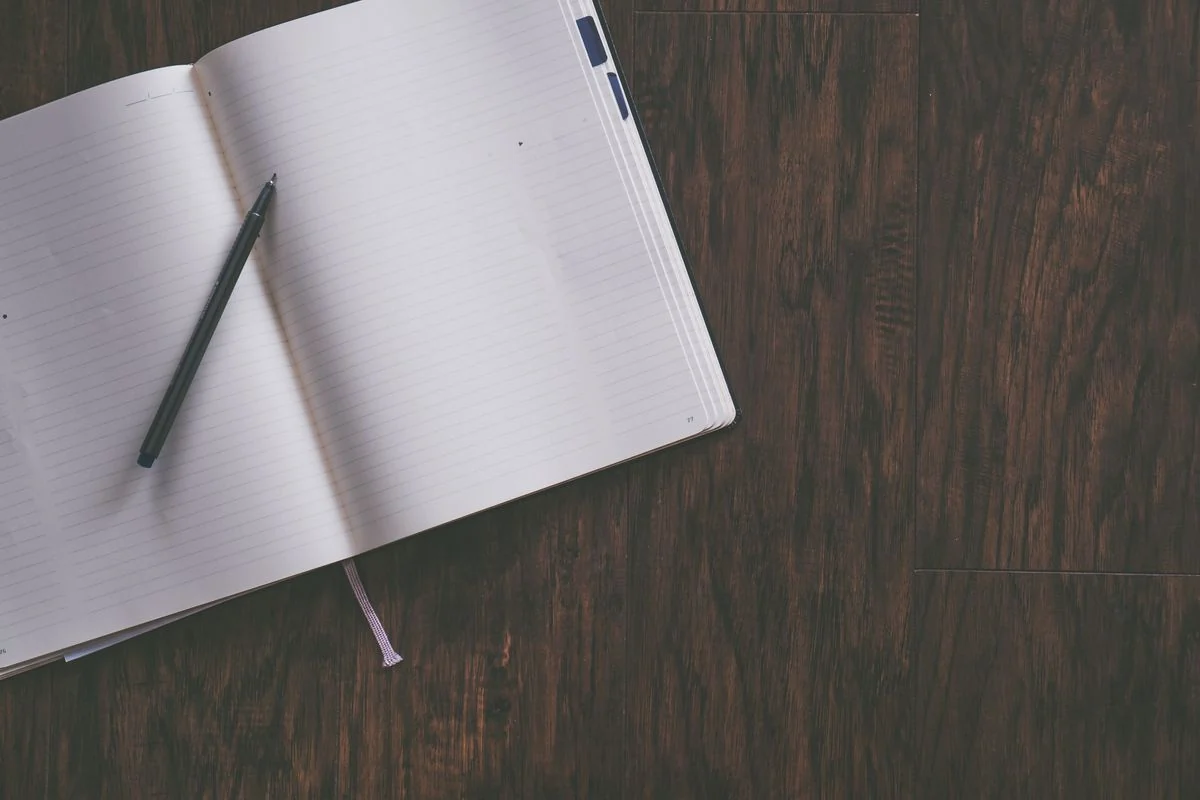 An open blank notebook with a pen on a wooden table