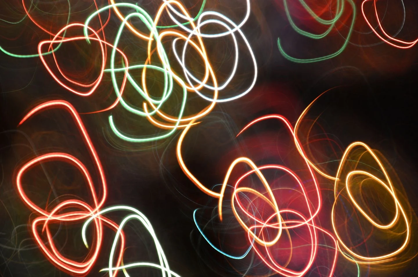 Red, green, yellow and white light trails forming loops against a dark background