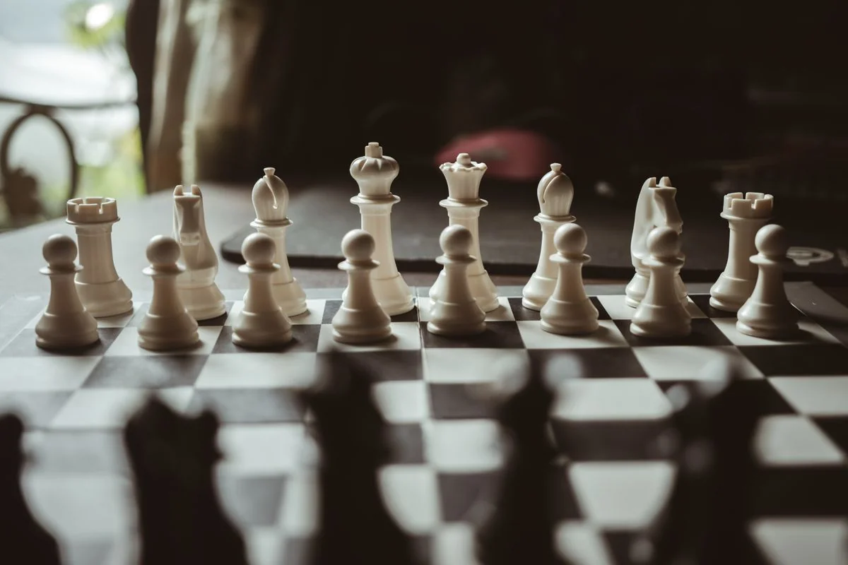 White chess pieces on a board with dark pieces blurred in the foreground